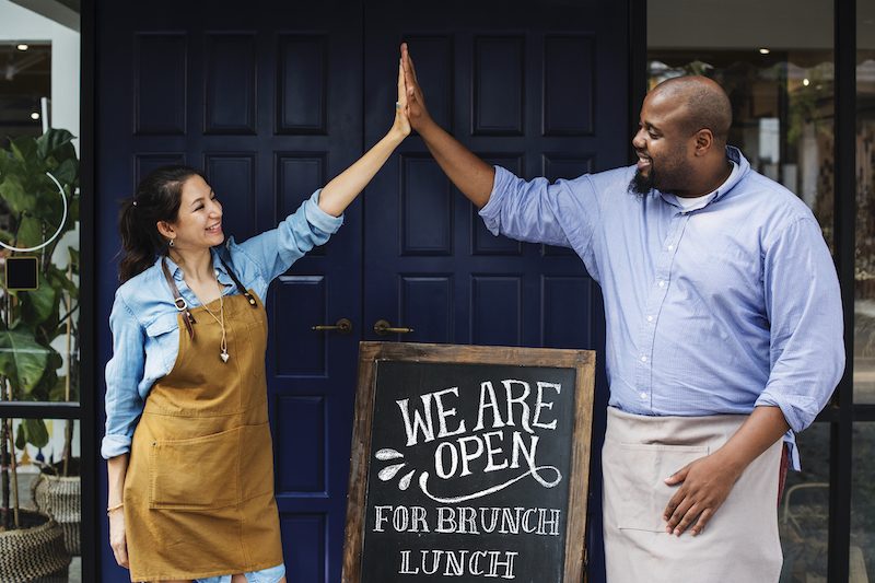 Cheerful business owners standing with open blackboard