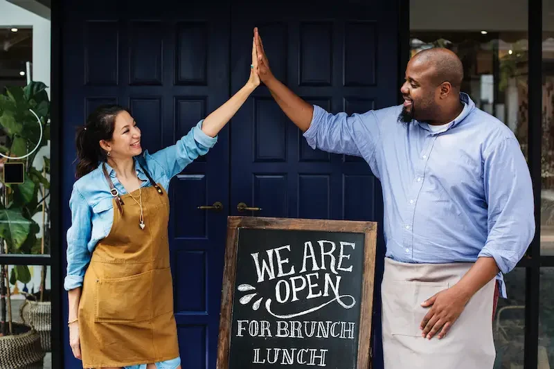 Cheerful business owners standing with open blackboard